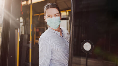 Eine Frau mit Maske steht in der Tür eines Busses.