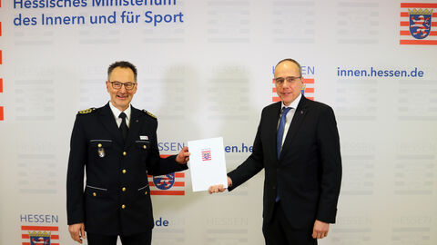 Bereitschaftspolizei Präsident Volker Pfeiffer wurde von Peter Beuth verabschiedet. Sie stehen nebeneinander und eine Urkunde wird überreicht.