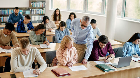 Ein Dozent unterstützt seine Studentinnen und Studenten in einem Seminarraum.