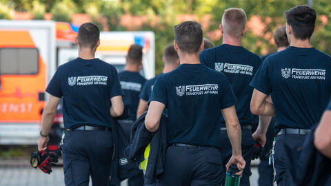 Mehrere Personen mit Shirts mit der Aufschrift "Feuerwehr Frankfurt am Main" laufen über ein Gelände.