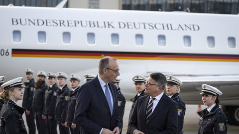 Zwei Männer stehen vor einem Flugzeug. Im Hintergrund stehen in zwei Reihen uniformierte Männer.