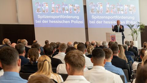 Eine Person steht auf der Bühne und hält eine Rede. Davor befindet sich Publikum.