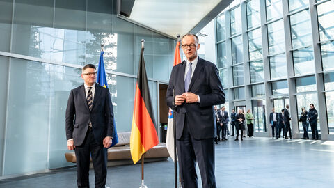 Zwei Männer stehen in einem großen Raum mit einer hohen Decke und metallischen Konstruktionen.