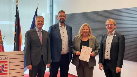 Vier Personen stehen nebeneinander und eine hält eine Urkunde in der Hand.